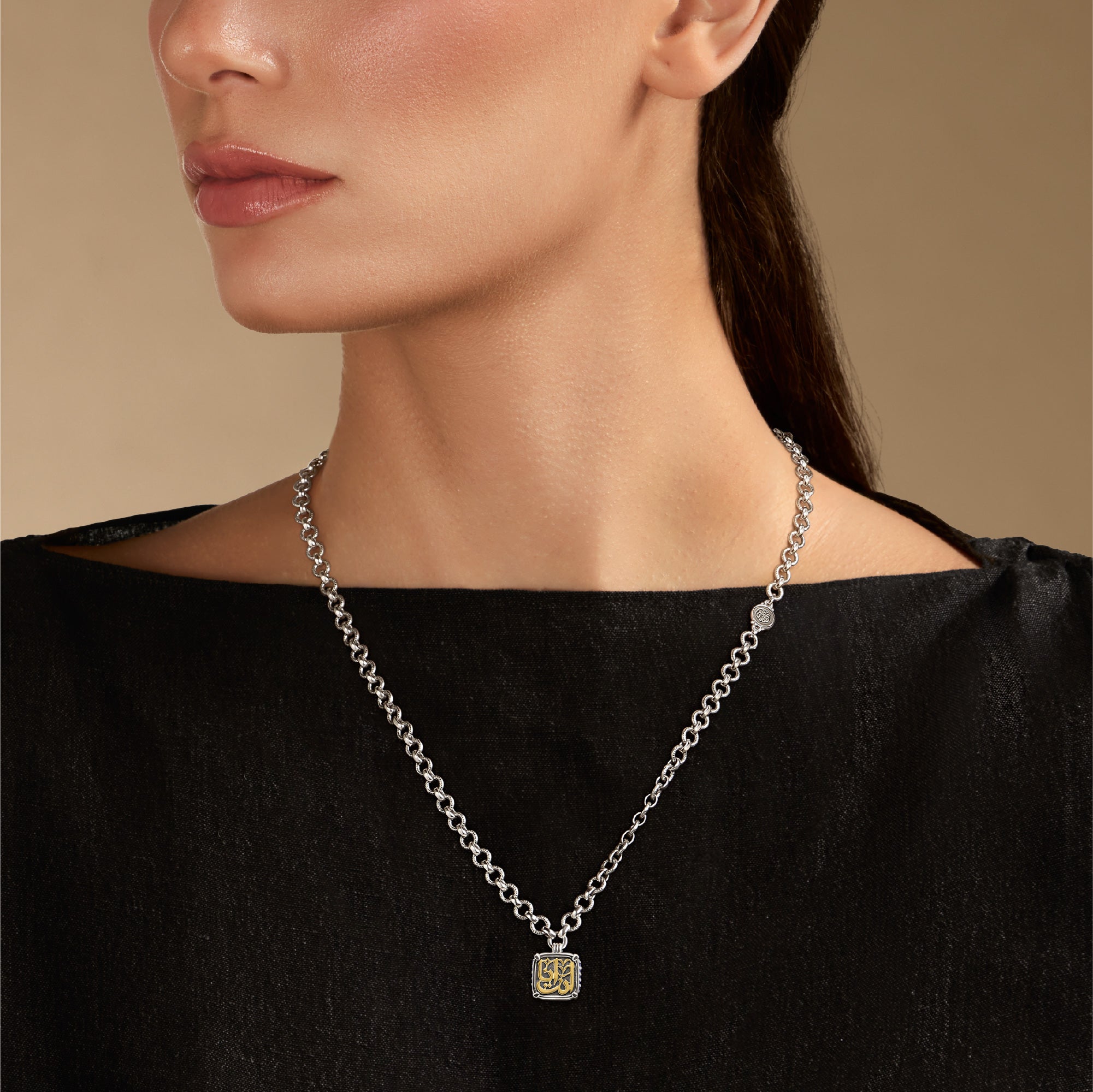 Silver necklace with a pendant worn by a person against a beige background