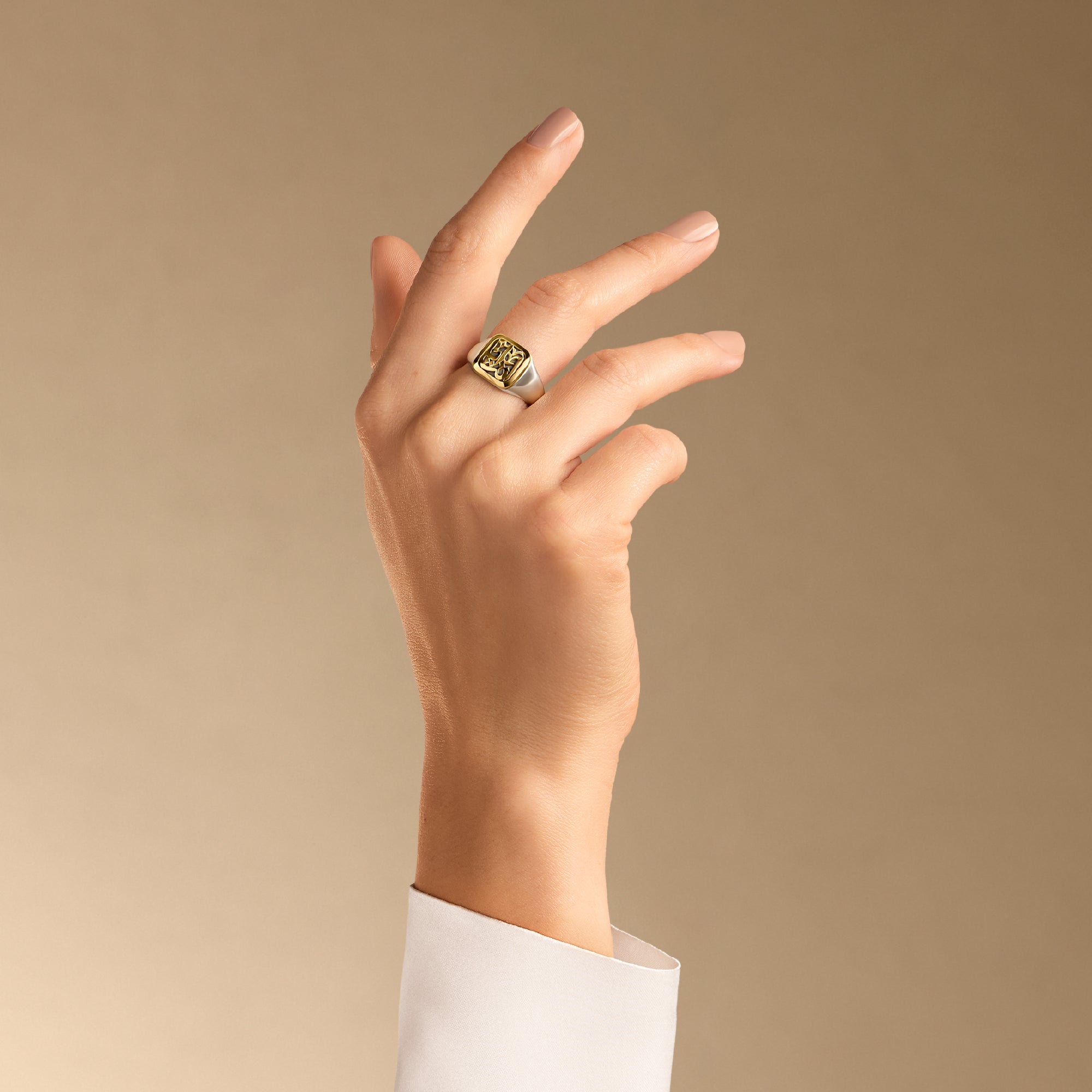 Hand wearing a gold ring on a beige background