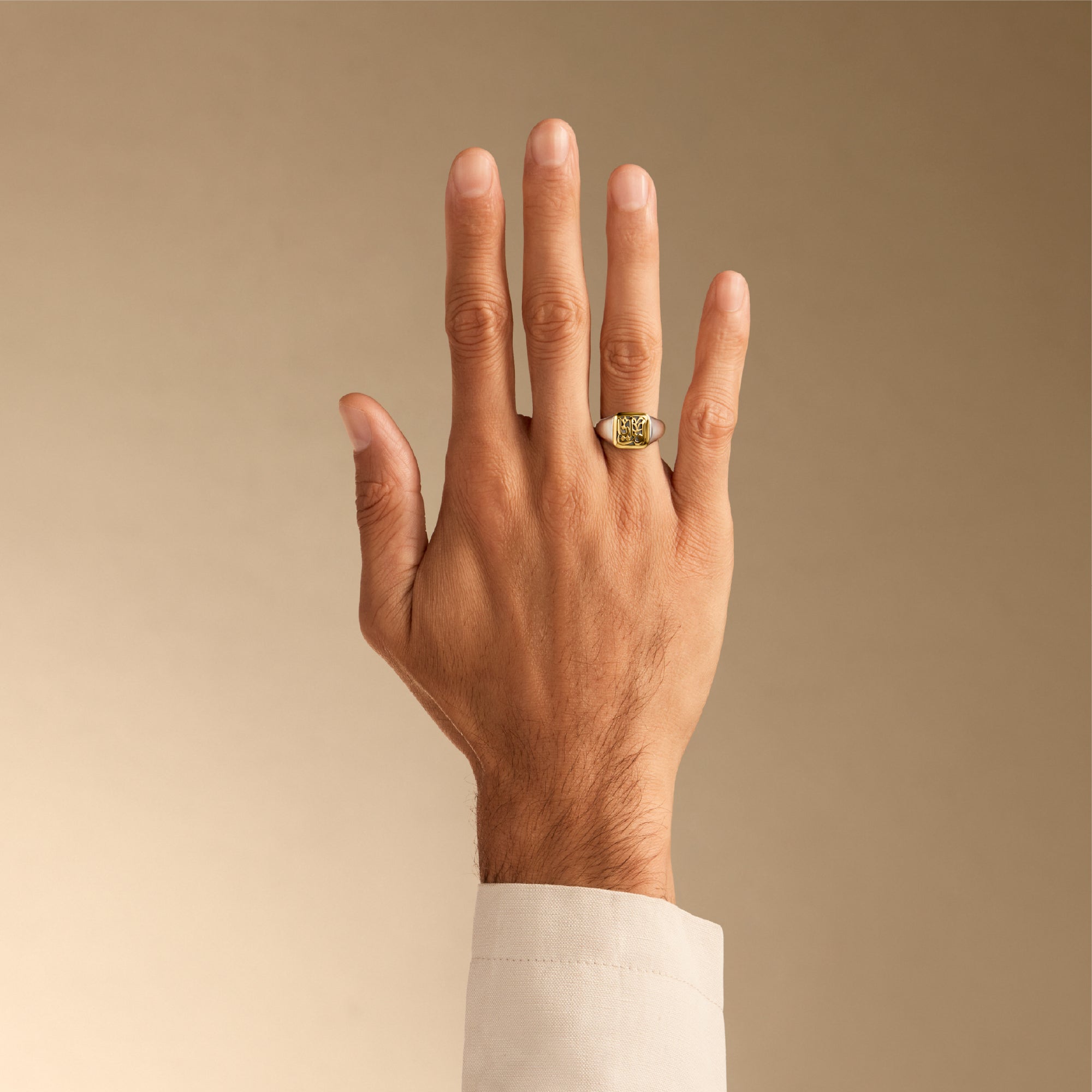 Hand wearing a gold ring on a beige background